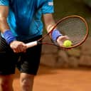 Close-up of a racket of a focused tennis player poised to serve the ball at the start of a match.