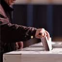A person's hand casting a vote into the ballot box during elections.
