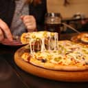 close-up of a female holding a slice of Italian pizza with mozzarella, olives, and basil at a pizzeria setting