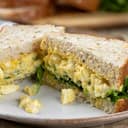 Close-up of a freshly made egg salad sandwich on whole grain bread, sliced in half and served on a plate.