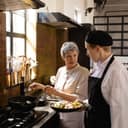older female chef talking with a younger male colleague who is holding a plate of chopped vegetables in a restaurant kitchen