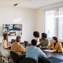 In-office team members having a meeting with remote colleagues on a large screen, modern office setup