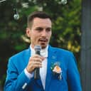 Man in blue suit holding microphone doing a wedding speech