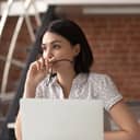 Asian businesswoman at her home office desk thinking about something, holding glasses in her hand with laptop in front of her