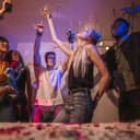Young men and women having fun at a colorful house party. Friends dancing in joy holding drinks at a house party.