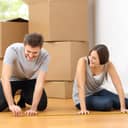 Couple measuring the floor with moving boxes in the background