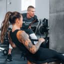 Woman at gym on a rowing machine alongside her personal trainer
