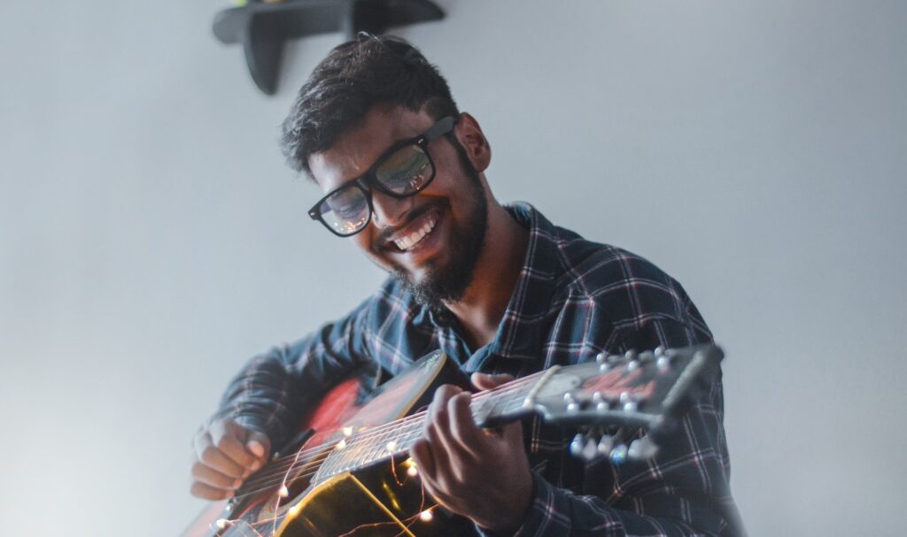 A young man smiling while playing the guitar with natural talent