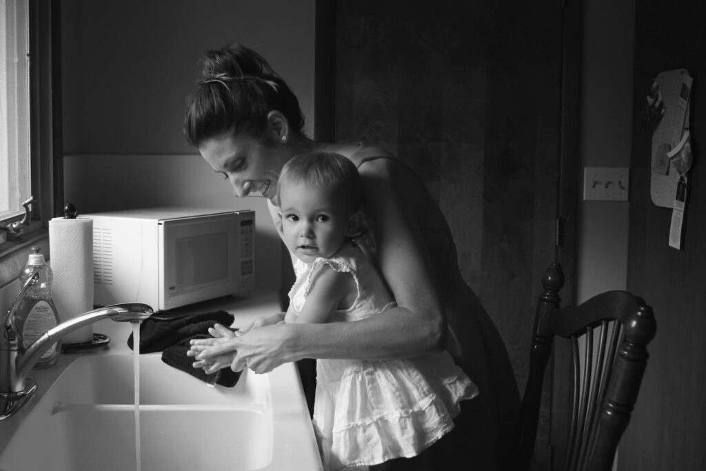 A mother washing her young daughter's hands in the kitchen sink