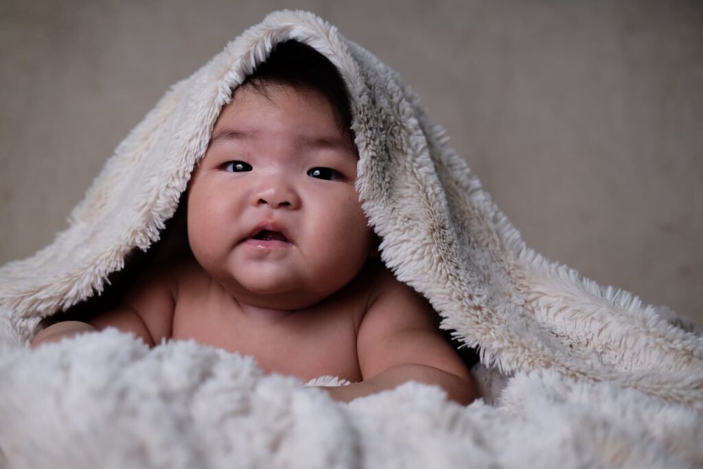A chubby baby looking out from underneath a fuzzy, white blanket