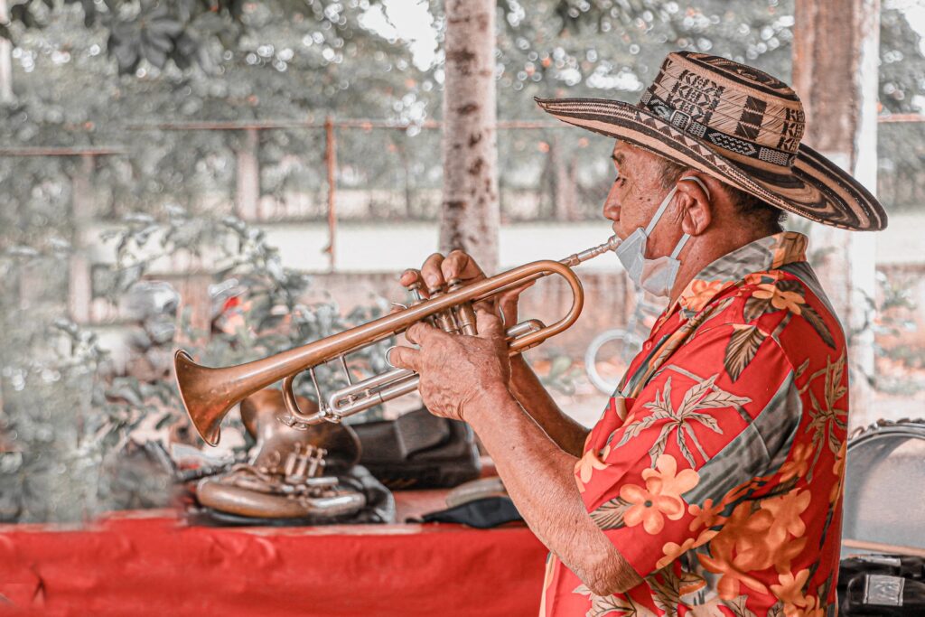 An older man in a hat and colorful shirt playing a trumpet