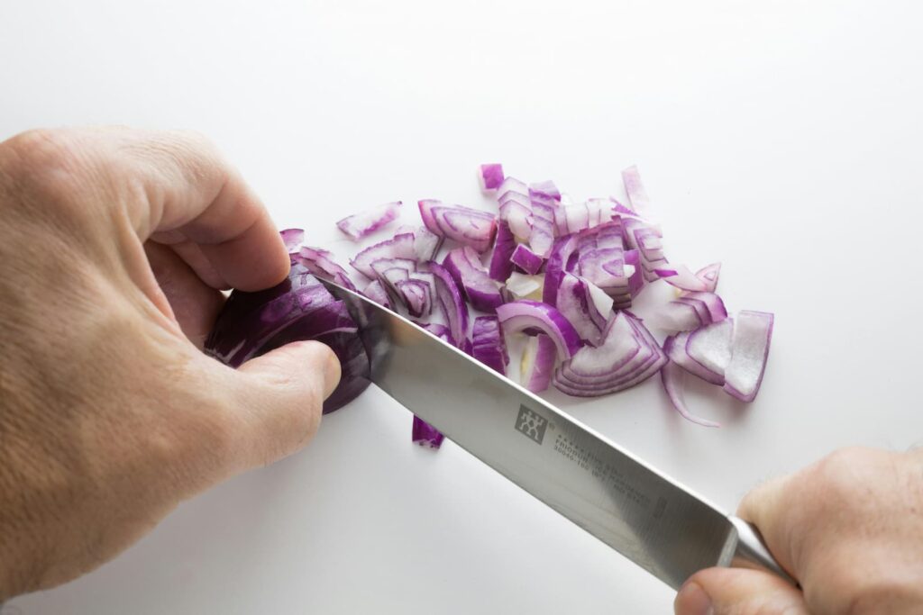 A pair of hands cutting an onion into small pieces