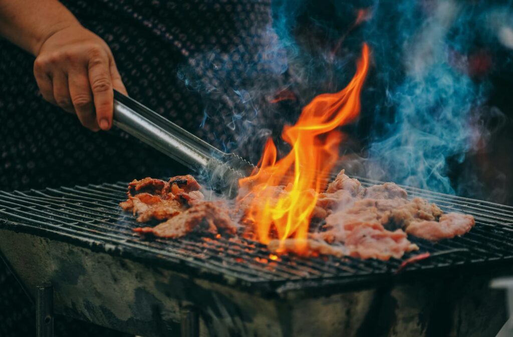 A person grilling meat outdoors