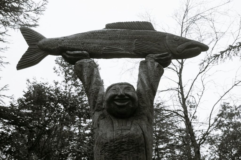 A wooden statue of a man holding a large fish above his head