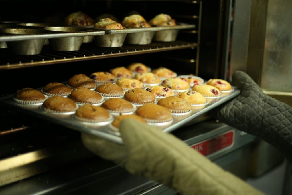 Someone pulling a tray of freshly baked muffins from an oven