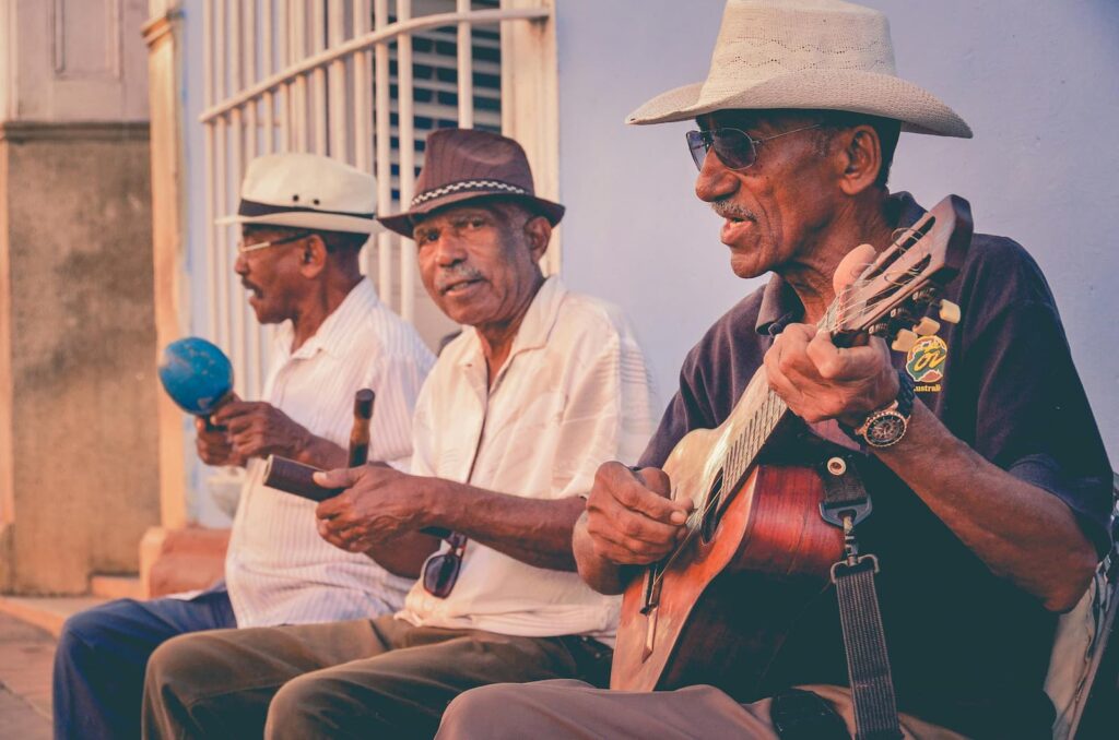 Three older men playing various instruments while sitting outdoors