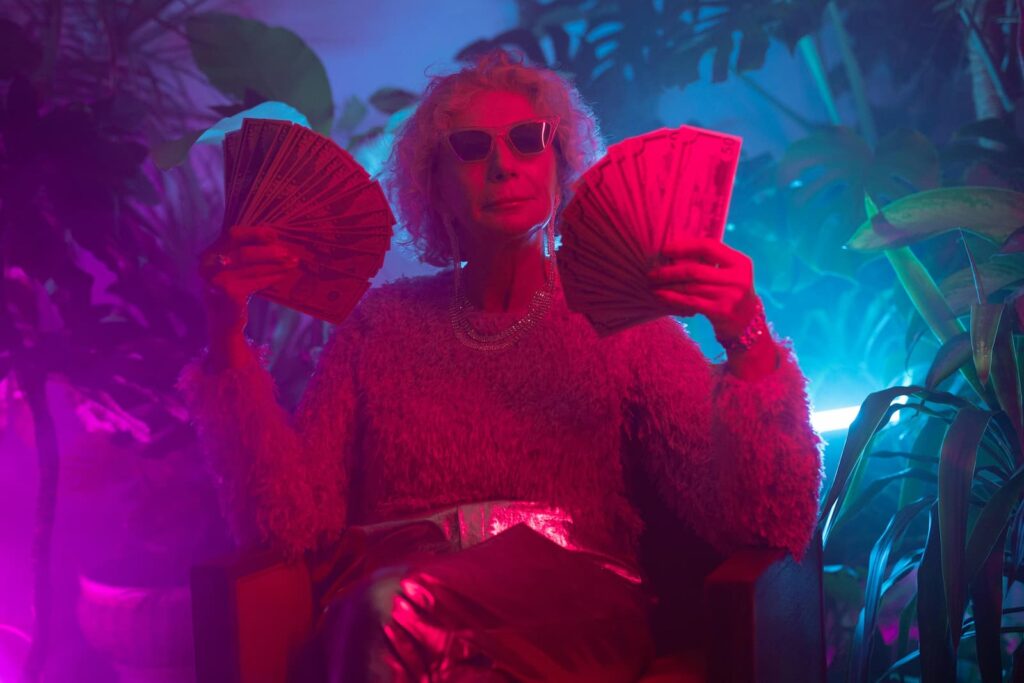 A rich older woman wearing sunglasses and holding lots of cash in both hands