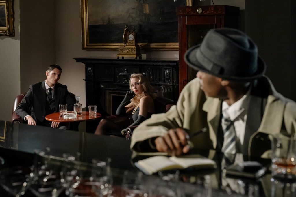 A detective sitting at a bar and looking over his shoulder at a pair of suspicious people