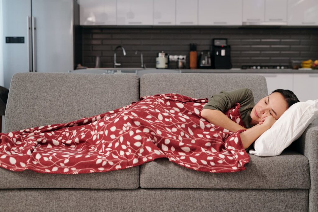 A woman sleeping on a couch under a red and white blanket