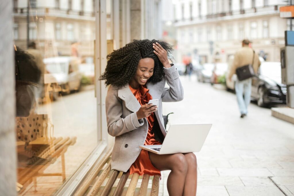 A young woman playing a word game on her phone while sitting on a bench on a city street