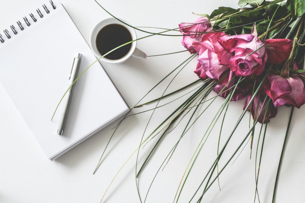A blank note pad on a white table next to a bouquet of flowers