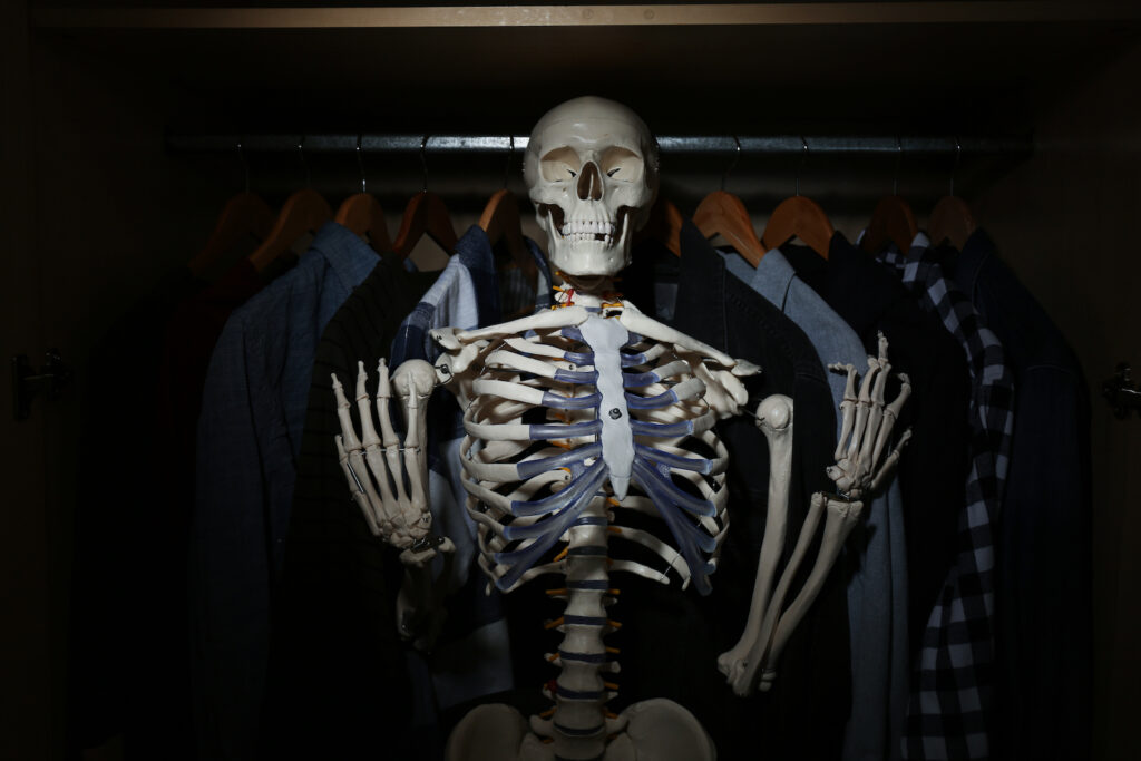 A skeleton surrounded by clothes in a closet