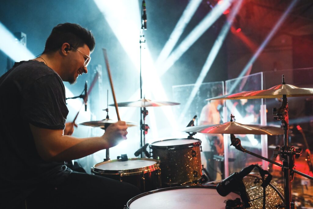 A young man playing the drums on stage with his bandmates