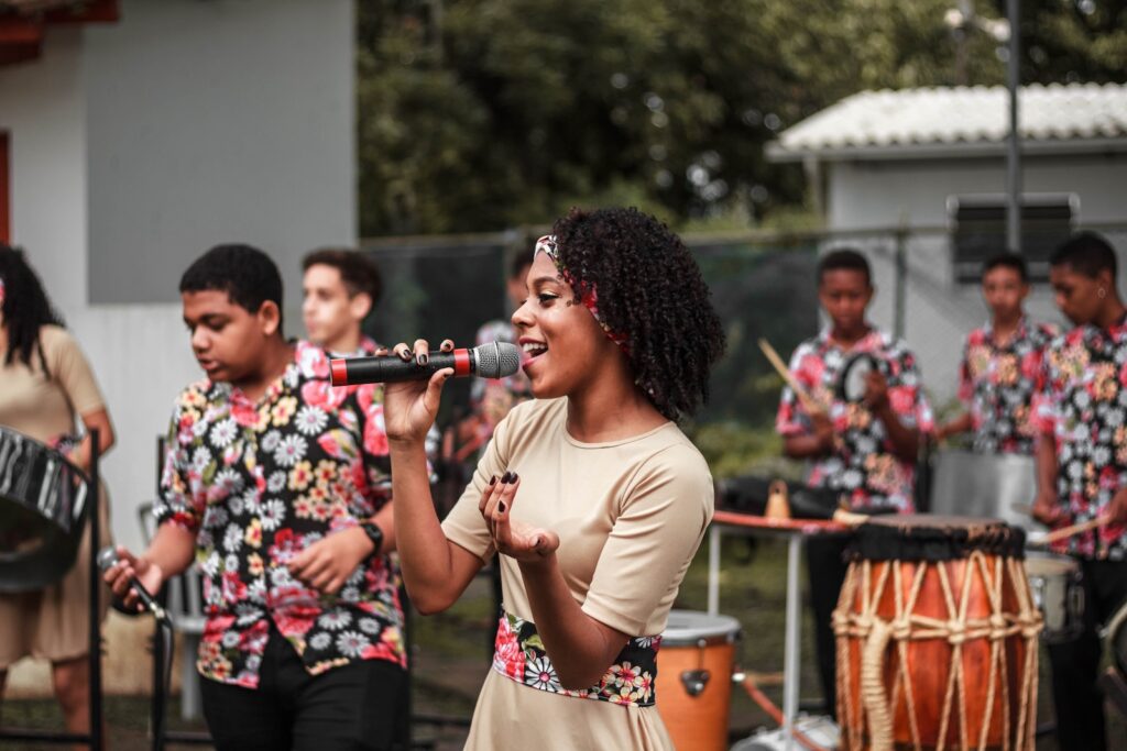 A young woman singing a tune in front of a large band playing percussion instruments