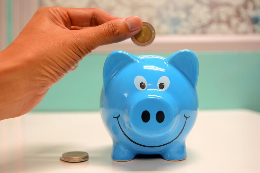 A woman's hand placing a coin into a blue piggy bank
