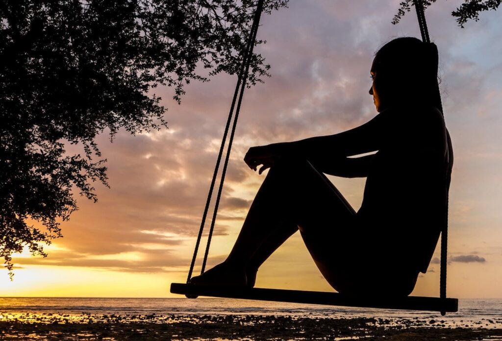 A woman sitting on a swing while watching the sunset of the ocean