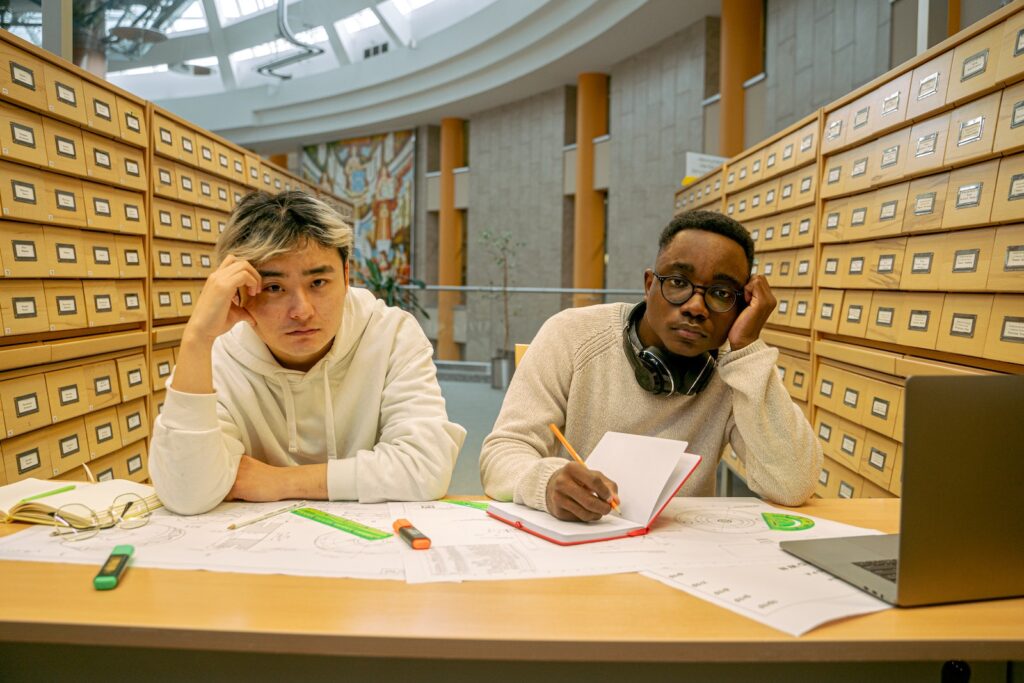 Two bored, jaded young men sitting in a library