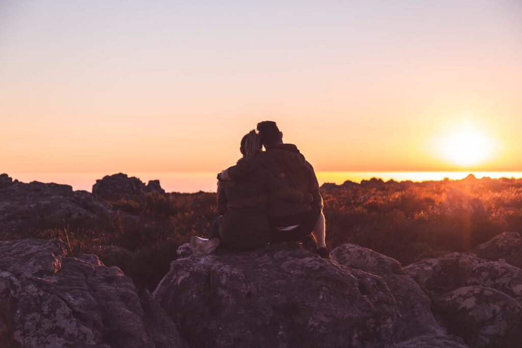 A couple sitting on a rock and watching the sun set
