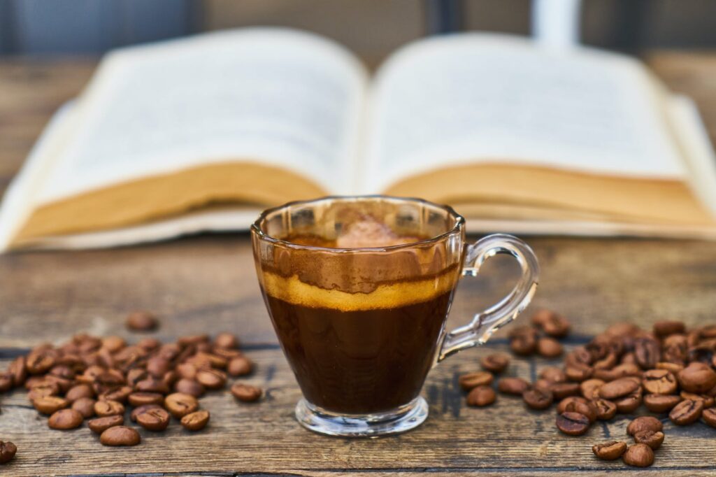 A cup of coffee surrounded by coffee beans and an open book