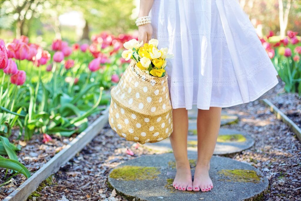 A woman in a white dress holding a basket of flowers in the middle of a flower garden