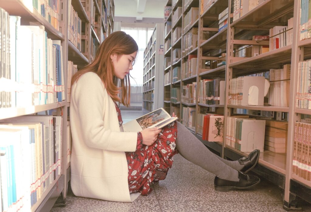 A young woman studying while sitting in the aisle of a library