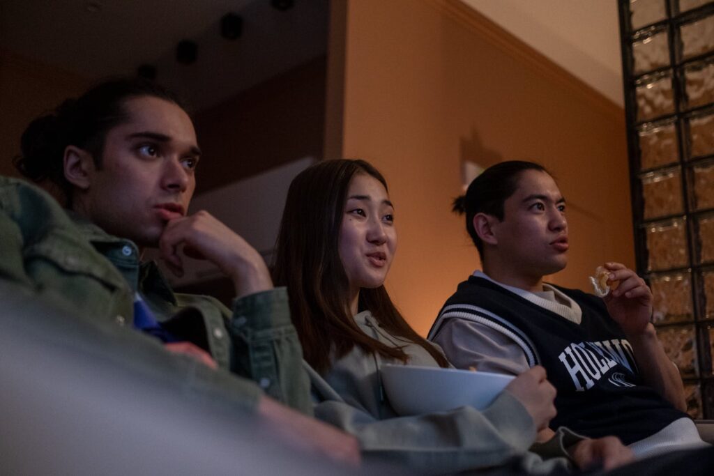 Three young people watching TV while eating snacks