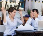 A woman throwing her hands up in the air while a man covers his face with hands in disapproving fashion