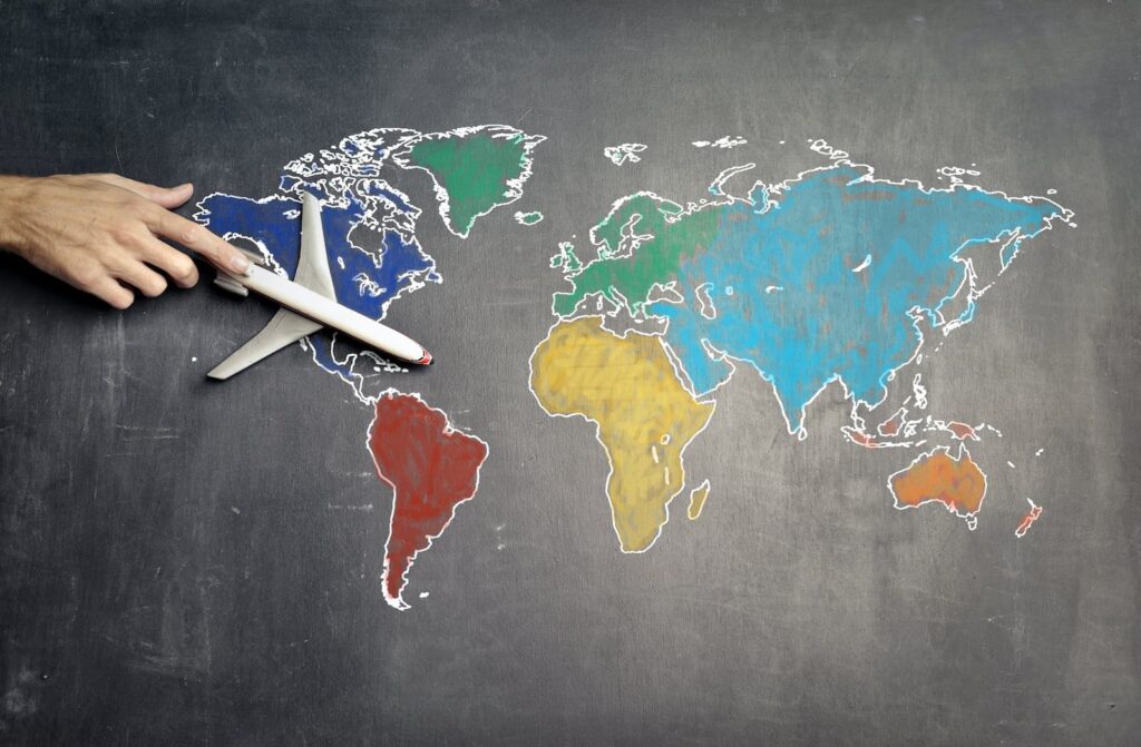A person's hand directing a miniature airplane over a drawing of the world's continents