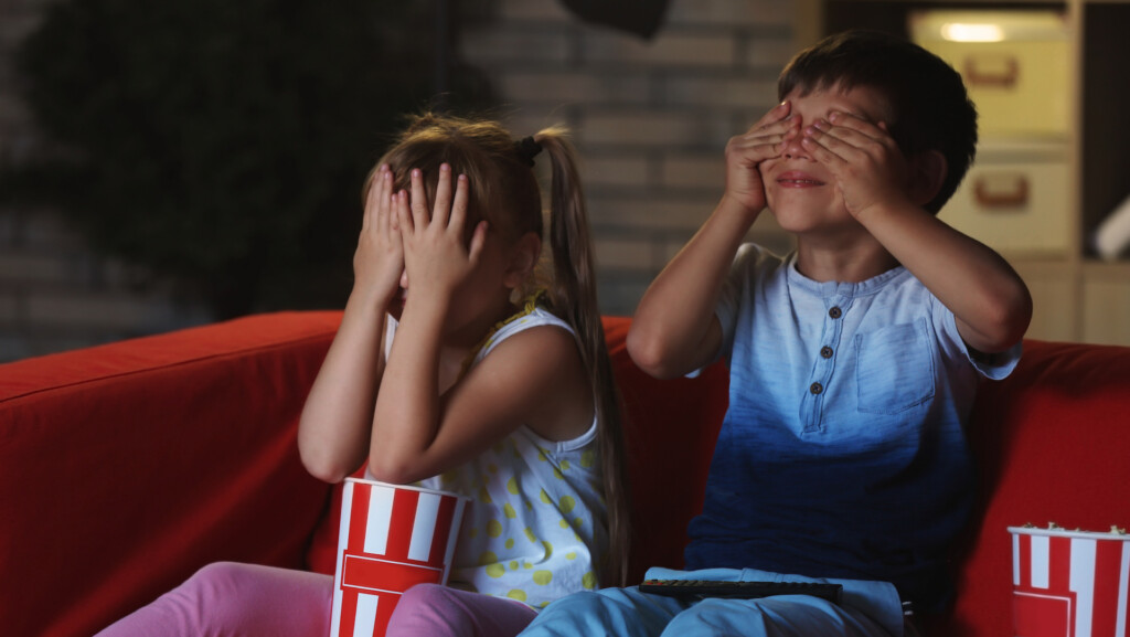 Children on a sofa watching a movie with an R rating