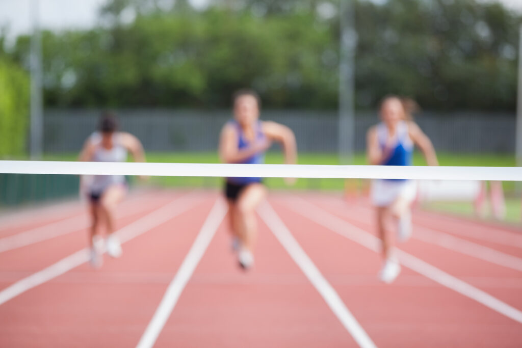 Three athletes running on a track toward a white finish line