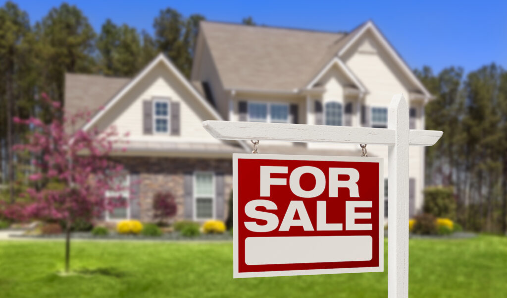 A "For Sale" sign in front of a large, white house
