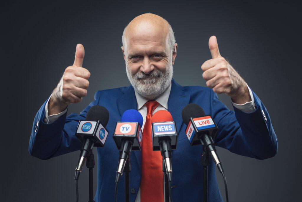 A politician giving "thumbs up" while standing in front of a row of microphones