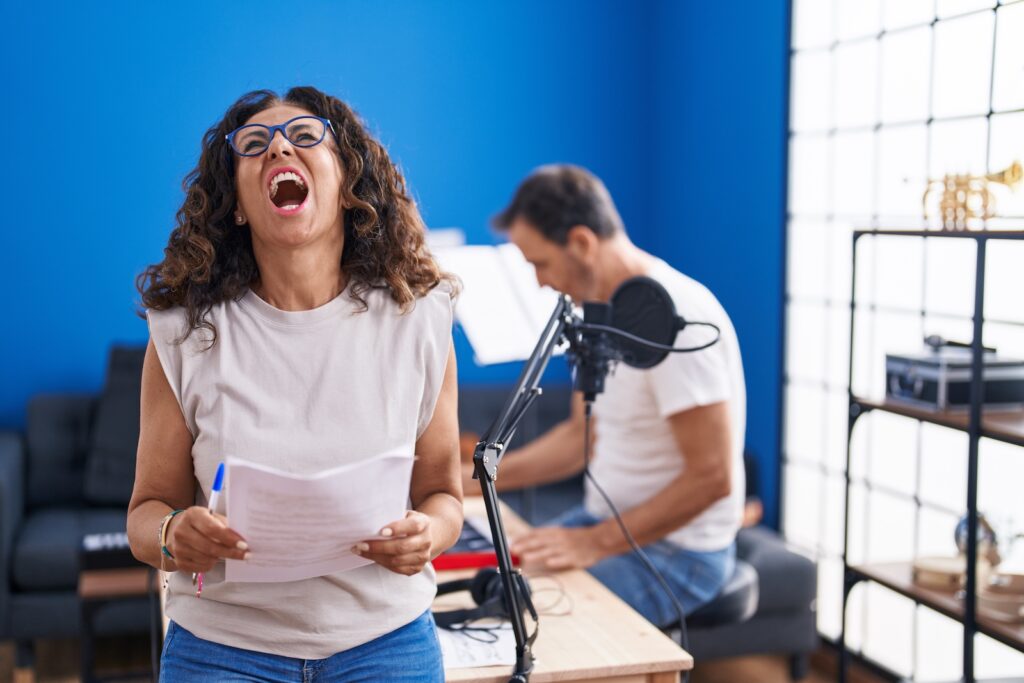 A tone-deaf woman in a music studio singing loudly and badly