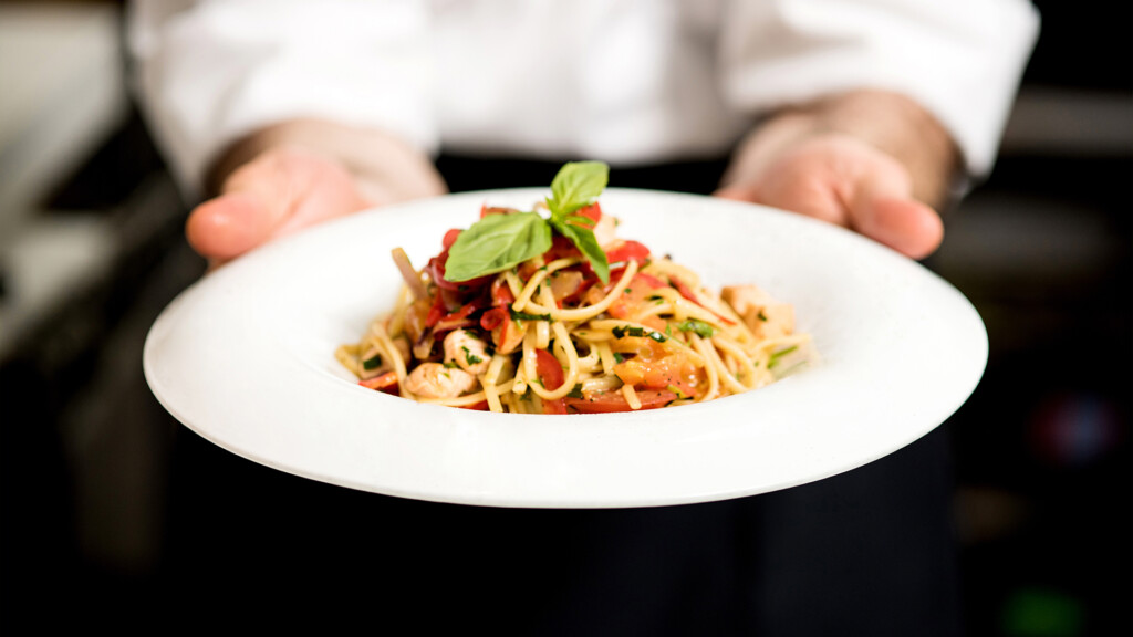 A chef in a restaurant presenting a plate of pasta he made