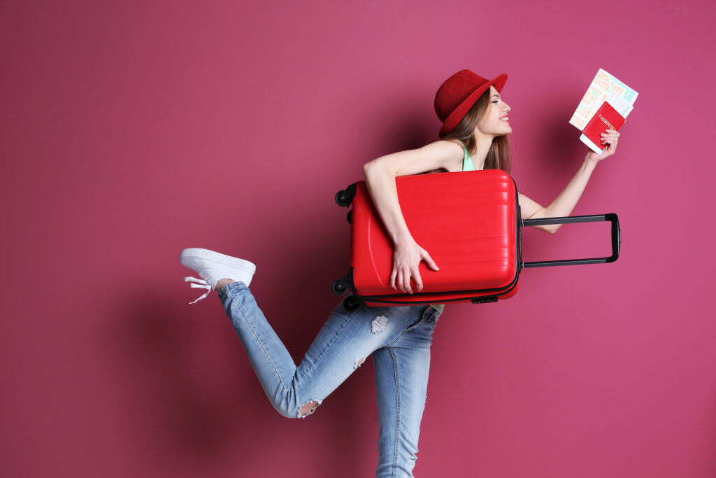 A smiling woman holding a suitcase and a passport against a magenta background