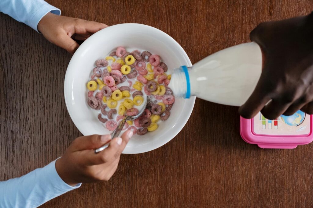 A man's hand pouring milk into a bowl of cereal held by a child