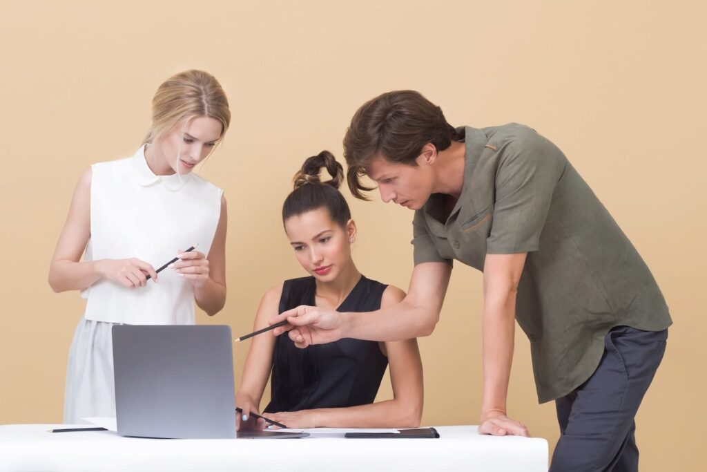 A man giving instructions to a woman seated in front of a laptop