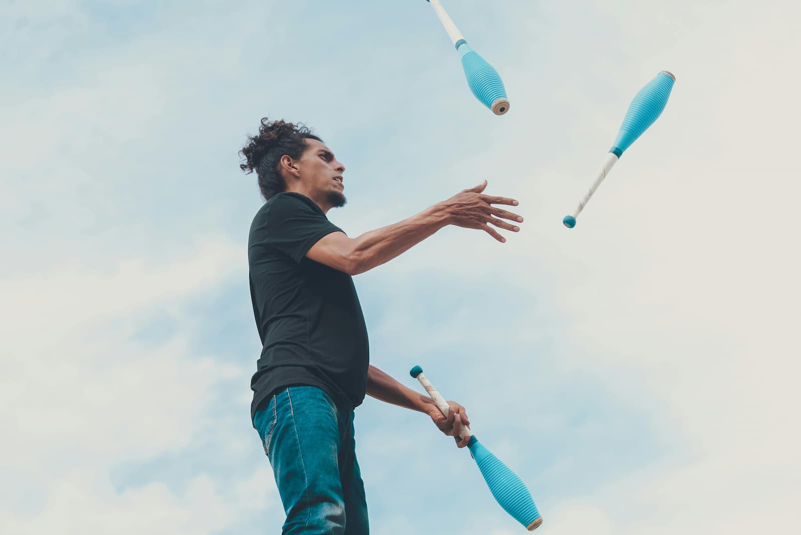 A man in a black t-shirt juggling three blue objects