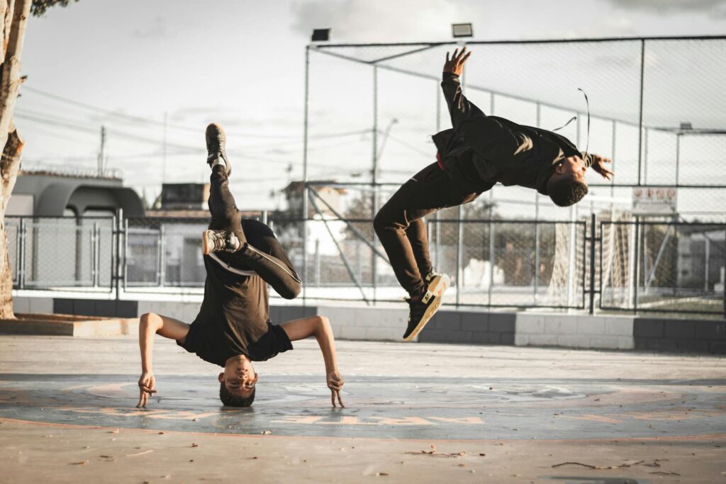 Two b-boys performing power moves in a city park